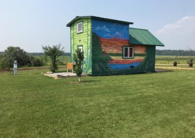 Colourfully painted rental cabin with nature-inspired mural, green metal roof and spacious grassy yard at French Creek RV in Fawcett, Alberta.