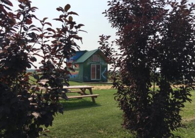 Rustic green rental cabin with picnic table and grassy yard framed by ornamental trees at French Creek RV in Fawcett, Alberta.